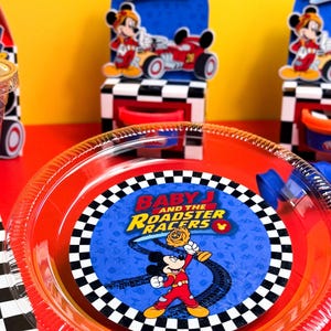 May include: Red plastic plate with a blue center featuring Mickey Mouse from "Baby and the Roadster Racers." The plate has a black and white checkered border. Party supplies are on a red surface.