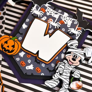 May include: A Halloween banner with a white letter W, a black and white mummy Mickey Mouse holding a jack-o-lantern, and a gray background with bats, spiders, ghosts, and skulls.