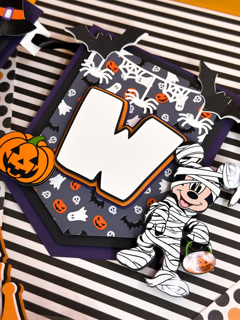 May include: A Halloween banner with a white letter W, a black and white mummy Mickey Mouse holding a jack-o-lantern, and a gray background with bats, spiders, ghosts, and skulls.
