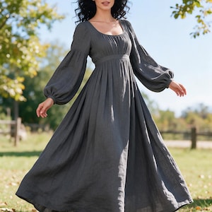 May include: A charcoal gray maxi dress featuring a square neckline, a fitted bodice with subtle gathering, and long, voluminous bishop sleeves with elasticized cuffs. The skirt is floor-length and flows from a defined waistline in a solid color.