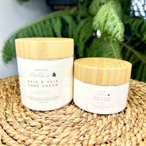 K&ouml;nnte beinhalten: Zwei Gl&auml;ser mit Haar- und Hautpflegecreme mit Bambusdeckeln. Das gr&ouml;&szlig;ere Glas ist mit "Barr & Co. PasPa's Hair & Skin Care Cream" beschriftet und das kleinere Glas mit "Barr & Co. PasPa's Hair & Skin Care Cream".
