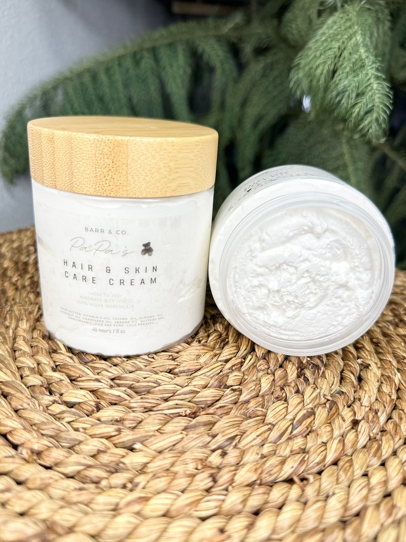 K&ouml;nnte beinhalten: Ein wei&szlig;es Glas mit Bambusdeckel, beschriftet mit "Barr & Co. Pai Pais Hair & Skin Care Cream" und einem kleinen B&auml;ren-Symbol. Das Glas ist mit einer wei&szlig;en Creme gef&uuml;llt und steht auf einer geflochtenen Matte.