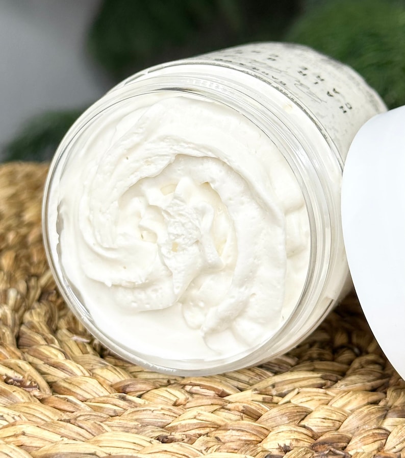 K&ouml;nnte beinhalten: Nahaufnahme von wei&szlig;er, geschlagenem K&ouml;rperbutter in einem durchsichtigen Glasgef&auml;&szlig;. Das Gef&auml;&szlig; steht auf einem geflochtenen Korb.