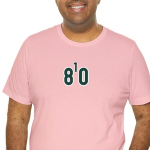 May include: A pink t-shirt with a green and white "8'0" graphic on the front.