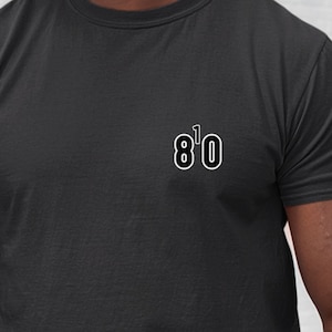 May include: A black t-shirt with the text "8'0" printed on the front in white.