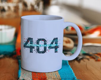 Könnte beinhalten: Weiße Keramik-Tasse mit einer schwarz-blauen Grafik mit der Aufschrift "404 CONVERSATION SKILLS NOT FOUND". Die Tasse hat einen gebogenen Henkel und steht auf einem farbenfrohen Untersetzer mit Fransen. Die Tasse steht auf einem Holztisch.
