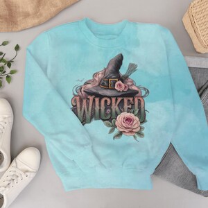 May include: A light blue sweatshirt featuring a graphic of a witch's hat, roses, and the word "WICKED" in a decorative font. The design includes bats and floral elements, perfect for Halloween or a witchy aesthetic.