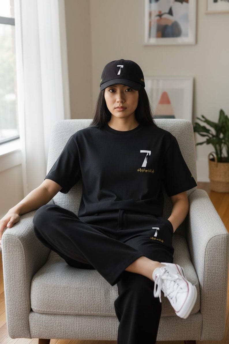 Puede incluir: Conjunto de camiseta, pantal&oacute;n y gorra de b&eacute;isbol negros con un gr&aacute;fico del n&uacute;mero 7 en blanco. La gorra y la camiseta presentan el n&uacute;mero 7 en blanco. Los pantalones tienen el n&uacute;mero 7 en blanco. El modelo lleva zapatillas blancas.