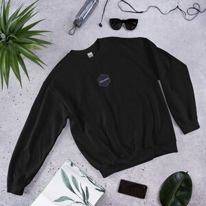 Op de afbeelding: Zwart sweatshirt met een zeshoekig logo met de tekst "tidyverse" in wit. Het logo heeft een zwarte achtergrond met witte sterren.