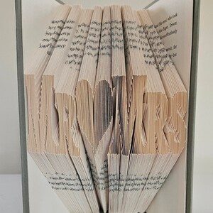 Peut inclure: Une sculpture d'art de livre avec le mot "LOVE" plié dans les pages. Le livre est ouvert et les pages sont pliées pour créer le mot. Le livre est sur une surface blanche.