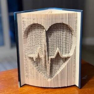 Peut inclure: Une sculpture d'art de livre en forme de cœur avec une ligne d'ECG à l'intérieur. Le livre est plié et superposé pour créer l'effet 3D.