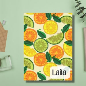 Könnte beinhalten: Ein Notizbuch mit einem bunten Muster aus Zitronen, Limetten und Orangen. Das Notizbuch trägt den Namen "Laila" auf der Vorderseite.