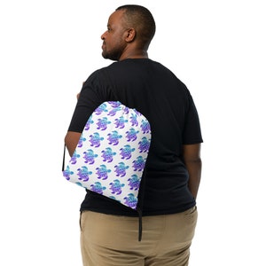 May include: A white drawstring bag with a repeating pattern of blue and purple sea turtles. The bag is being worn by a person.