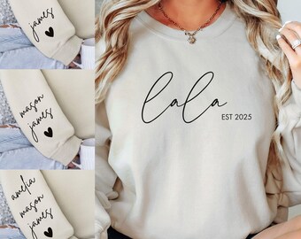 May include: A cream-colored sweatshirt with the text "lala est 2025" on the front. The sweatshirt has long sleeves and a crew neck.