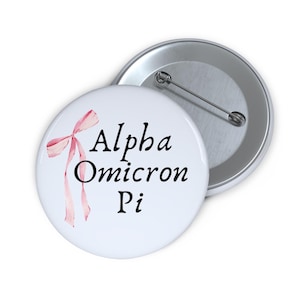 May include: White button with a pink ribbon and the text "Alpha Omicron Pi" in black.