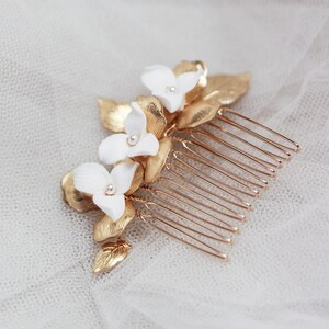 May include: A decorative hair comb with white flower details and crystal centres, set amongst gold-coloured leaves. The comb has gold-coloured tines. This elegant hair accessory is suitable for weddings or special occasions.