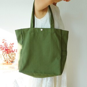 May include: Olive green canvas tote bag with two exterior pockets and a silver snap closure. The bag has two sturdy handles for carrying. The tote bag is a simple, yet stylish accessory.