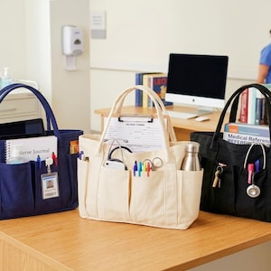 Puede incluir: Tres bolsos de mano en azul marino, crema y negro sobre una mesa de madera. Cada bolso tiene m&uacute;ltiples bolsillos y est&aacute; lleno de suministros m&eacute;dicos, cuadernos y bol&iacute;grafos. Una mujer con uniforme azul est&aacute; al fondo.