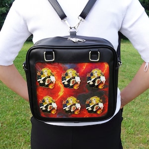 May include: Black square crossbody bag with a colorful graphic of a character on the front. The bag has a top handle and adjustable black straps. The graphic features a character with yellow hair and a black uniform.
