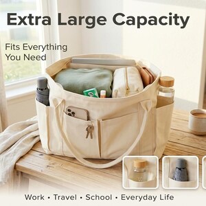 Puede incluir: Bolso tote color crema con m&uacute;ltiples bolsillos, lleno de art&iacute;culos como un port&aacute;til, un su&eacute;ter y una botella de agua. La bolsa tiene el texto "Extra Large Capacity" y "Fits Everything You Need". La parte inferior de la imagen tiene las palabras "Work &bull; Travel &bull; School &bull; Everyday Life".