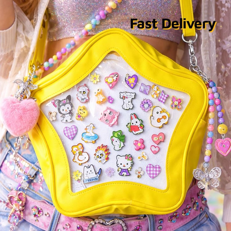 May include: A bright yellow star-shaped purse with a clear front panel filled with colorful cartoon character pins. The purse has a long strap and is accessorized with a pink heart-shaped charm and a beaded strap. The text "Fast Delivery" is visible.