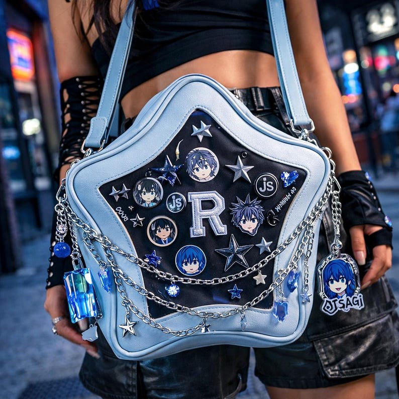 May include: A light blue star-shaped shoulder bag with a black center panel. The bag features silver chains, star-shaped charms, and character pins. The letter "R" is prominently displayed. The bag is decorated with anime-style character art.