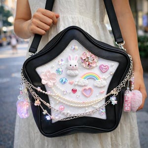 May include: Black star-shaped handbag with a white interior decorated with a bunny, rainbow, hearts, and flowers. The bag has a black strap and silver chain accents with dangling charms and a pink pom-pom.