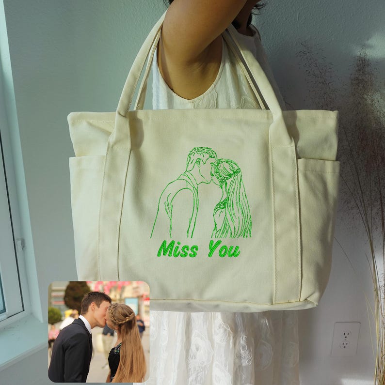 Puede incluir: Bolso tote color crema con un dise&ntilde;o bordado en verde de una pareja bes&aacute;ndose y las palabras "Miss You". El bolso tiene dos bolsillos exteriores y asas resistentes. Una peque&ntilde;a foto de una pareja bes&aacute;ndose est&aacute; en la esquina inferior izquierda.