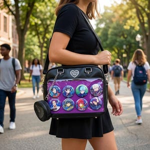May include: Black shoulder bag with a clear front pocket displaying colorful character pins. The bag has a heart-shaped emblem and a small, round coin purse attached. The bag is carried on a shoulder strap.