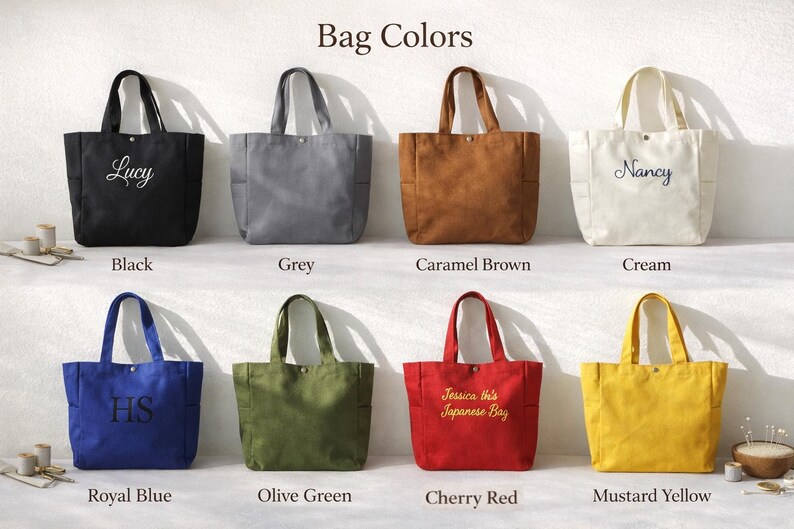 May include: A collection of eight tote bags in various colors, including black, grey, caramel brown, cream, royal blue, olive green, cherry red, and mustard yellow. Each bag has a rectangular shape with two handles and a pocket. Some bags have embroidered text.