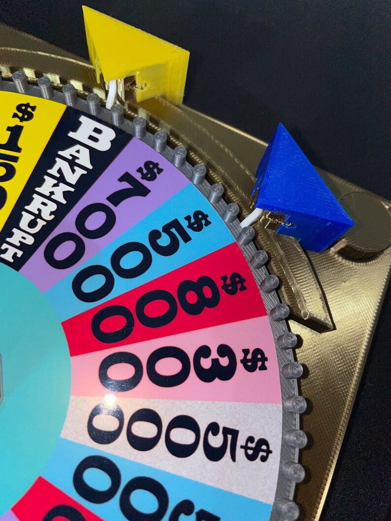 May include: A colourful wheel game with a spinning arrow. The wheel has different dollar amounts and the word "Bankrupt". The arrow is blue and yellow.