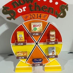May include: A colorful display with the words "now or then" and "2014" on top. The display features various food products, including Jell-O, Wheat Thins, and Classico, each with a price tag.