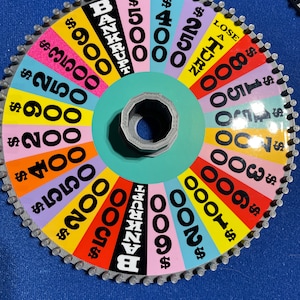 May include: A colourful wheel game with a spinning arrow. The wheel has different dollar amounts, including &pound;900, &pound;3500, &pound;250, &pound;900, &pound;200, &pound;400, &pound;550, &pound;200, &pound;500, &pound;400, &pound;250, &pound;1000, &pound;150, &pound;300, &pound;100, &pound;200, and &pound;600. The wheel also has the words "BANKRUPT" and "LOSE A TURN".
