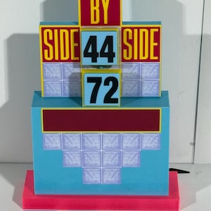 Puede incluir: Un set de juego de un programa de televisión azul y amarillo con las palabras "Side by Side" y los números "44", "72", "35", "51", "68" y "89".