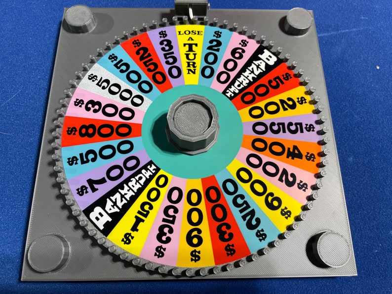 May include: A colourful wheel of fortune game with a spinning wheel and a grey base. The wheel has different dollar amounts and the phrase "Lose a Turn".