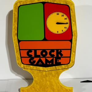 Puede incluir: Un juego de mesa vintage "Clock Game" con un marco amarillo. El juego presenta un cuadrado verde, una esfera de reloj roja y amarilla y rayas naranjas con las palabras "CLOCK GAME" en negro.