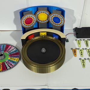 May include: A 3D-printed game wheel with a colorful numbered wheel, a spinning wheel, and three smaller wheels with red, yellow, and blue centers. Includes small signs with words like "Bike", "Car", and "Trip".