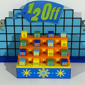 Puede incluir: Un colorido accesorio de programa de juegos con un diseño azul y naranja. El accesorio presenta un fondo de cuadrícula, un letrero que dice "1/2 Off" y dieciséis cajas numeradas. Se utilizan explosiones de estrellas doradas como decoración.