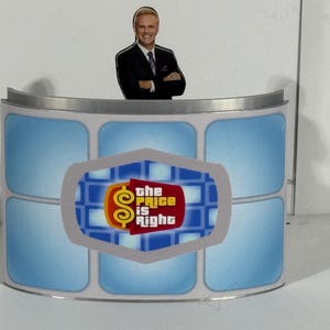 Puede incluir: Un escenario curvo con un diseño de azulejos azules y blancos. El escenario tiene una parte superior plateada y un logotipo que dice "the price is right" con un signo de dólar.