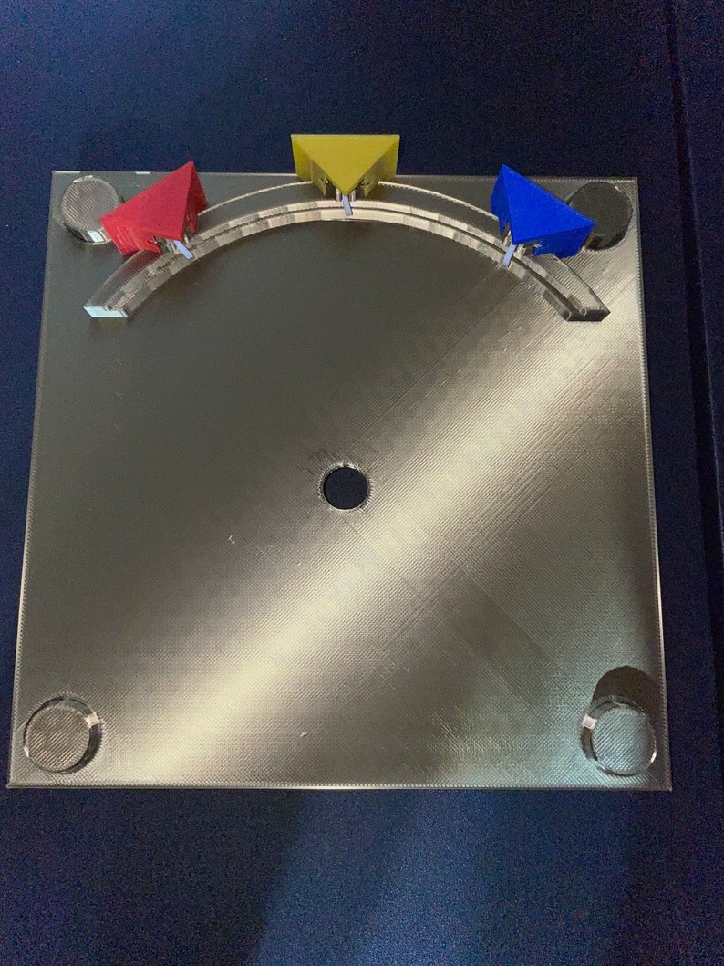 May include: A gold-coloured metal base with a circular hole in the centre. Three triangular pieces are attached to the base, one red, one yellow, and one blue.