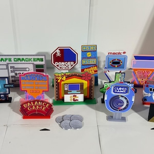 May include: A collection of colorful, miniature game show props featuring various titles like Safe Crackers, Danger Price, Balance Game, Back to 74, Clock Game, and On the Nose. These small, upright cardboard displays include printed text and graphics.