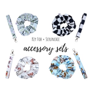 May include: Four accessory sets, each containing a fabric key fob with a metal clasp and a matching fabric scrunchie. The patterns include green leaves, black and white checkers, cartoon characters on white, and cartoon characters on light blue.