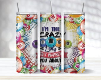 May include: A white tumbler with a straw, decorated with colourful bingo balls and cards. The text "I'M THE CRAZY BINGO Lady HEY WARNET YOU ABOUT" is displayed. A fun gift for bingo enthusiasts.