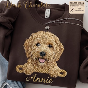 May include: A dark chocolate brown sweatshirt with a detailed embroidered-look image of a golden doodle dog and the name "Annie" in gold script. The sweatshirt has a crew neck and a small silver necklace. The text "Printed Design Embroidery Look Not Embroidered" is visible.
