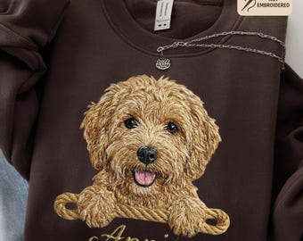 以下が含まれることがあります： 濃いチョコレートブラウンのスウェットシャツ。金色の文字で「Annie」と名前が入った、ゴールデン・ドゥードゥルの犬の刺繍風の画像が描かれています。スウェットシャツはクルーネックで、小さなシルバーのネックレスが付いています。「Printed Design Embroidery Look Not Embroidered」の文字も表示されています。