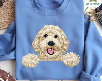 以下が含まれることがあります： ピンクの舌を持つ薄茶色のゴールデン・ドゥードゥル犬の刺繍デザインが施されたカロライナブルーのスウェットシャツ。犬の足が見え、下部には筆記体で「Carolina Blue」と書かれています。スウェットシャツはクルーネックです。