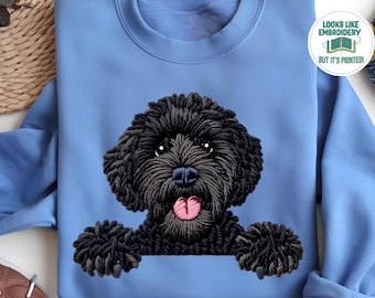 May include: Carolina Blue sweatshirt featuring a black dog graphic with a pink tongue. The dog appears to be embroidered. The text "Looks like embroidery but it's printed!" is in a circle on the upper right. The text "Carrolina Blue" is at the bottom.