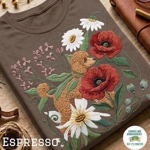 Op de afbeelding: Espresso-kleurig T-shirt met een geborduurd ontwerp van een poedel omringd door bloemen, waaronder rode klaprozen en witte madeliefjes. De tekst "ESPRESSO" staat linksonder. Het shirt heeft een ronde hals.