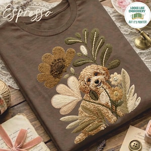 May include: A brown t-shirt featuring a printed design of a curly-haired puppy surrounded by embroidered-style flowers and leaves. The graphic includes two small flowers with smiley faces and the word Espresso written in cursive script at the top.