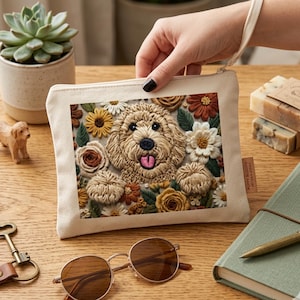 May include: A beige canvas zipped pouch with an embroidered dog surrounded by flowers in shades of brown, yellow, and white. The pouch has a small fabric loop and the text "PUPPY BLOOM" on a small tag.